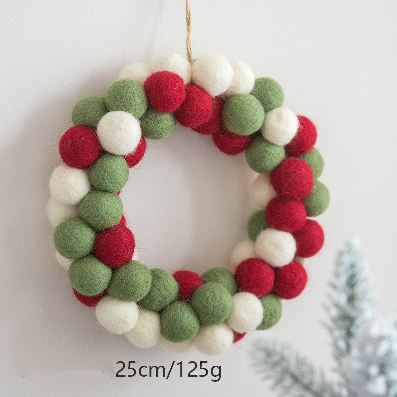 A festive wreath made of red, green, and white felt balls hangs on a wall. It measures 25cm in diameter and weighs 125g. A pine branch is visible in the foreground.