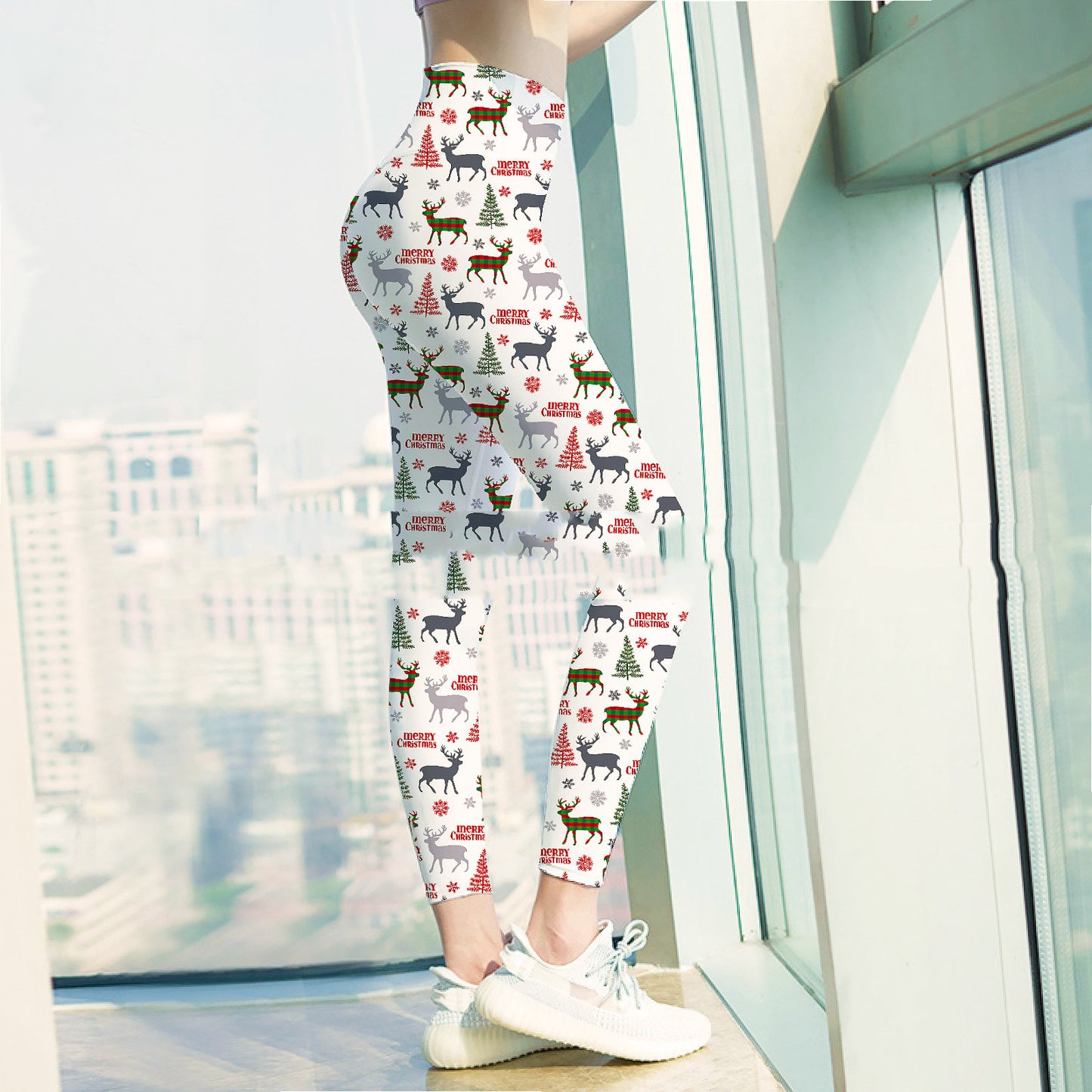 A person stands by a window wearing festive leggings with Christmas trees, reindeer, and "Merry Christmas" text, paired with white sneakers. The cityscape is visible outside.