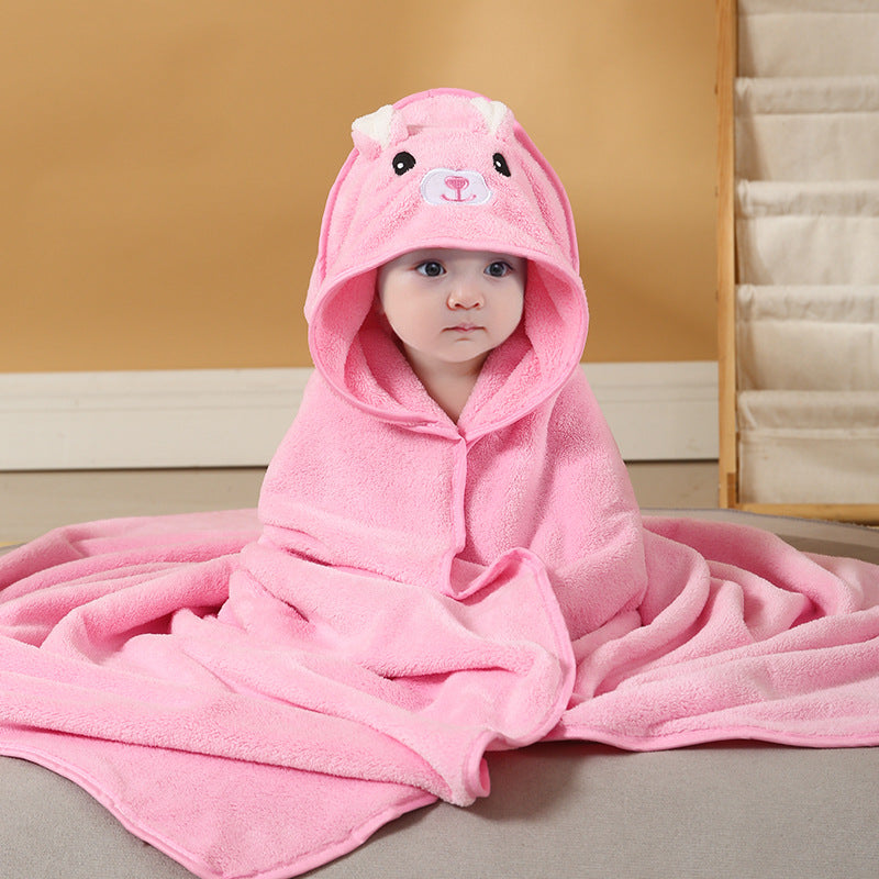 Baby wrapped in a pink towel with a bear hood, sitting on a gray surface against a beige background. The hood has ears and a cute bear face design.