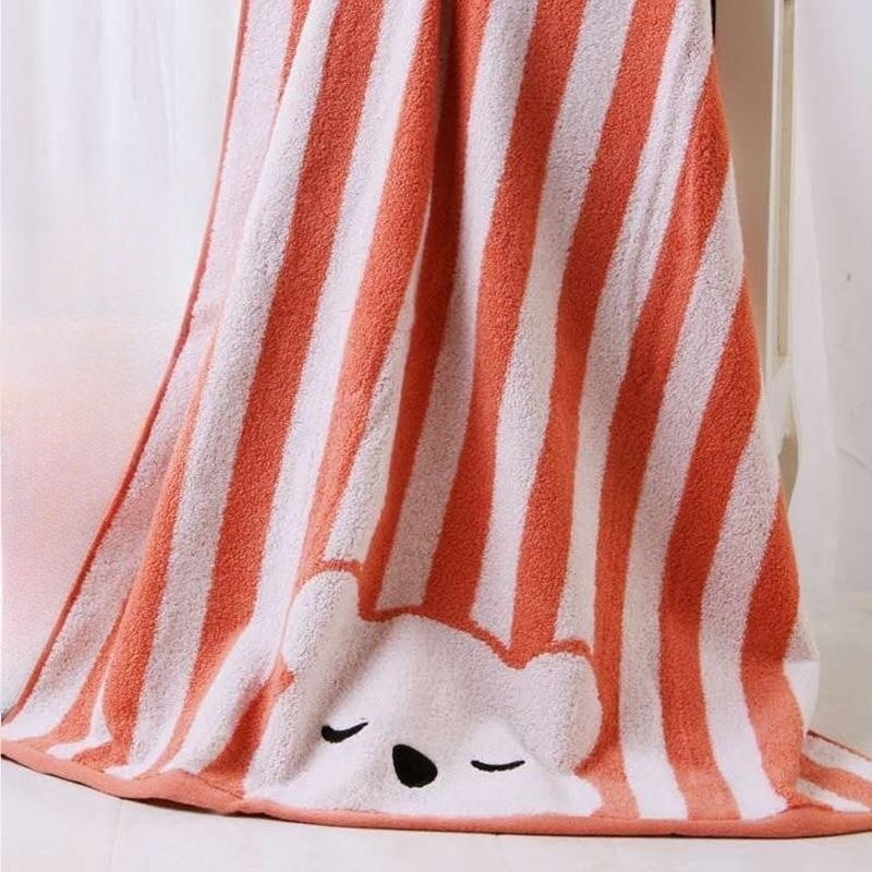A soft, plush towel with orange and white stripes features a cute, sleeping bear face at the bottom.