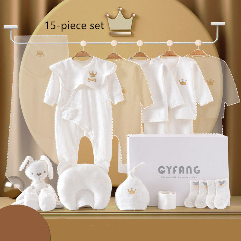 "Baby clothing set on hangers, featuring white onesies, jackets, a plush toy, pillow, hat, and socks. The 15-piece set is neatly arranged with a decorative crown theme."