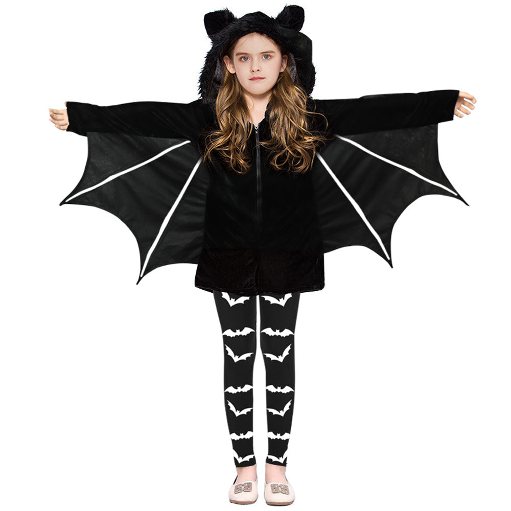 Young girl in a black bat costume with hood and wings extended. She wears leggings with white bat patterns and simple shoes, standing against a white background.