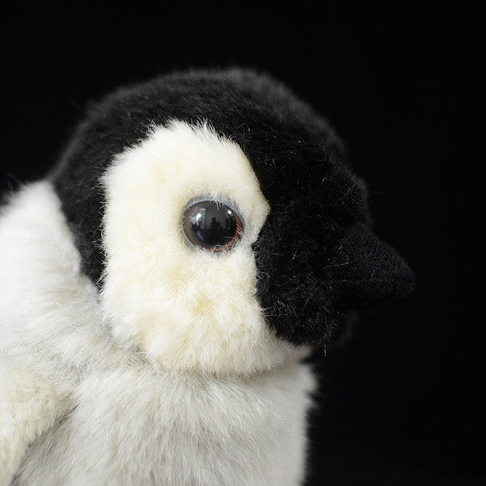 Close-up of a plush toy penguin with a black head, white face, and shiny, round eyes, set against a dark background.