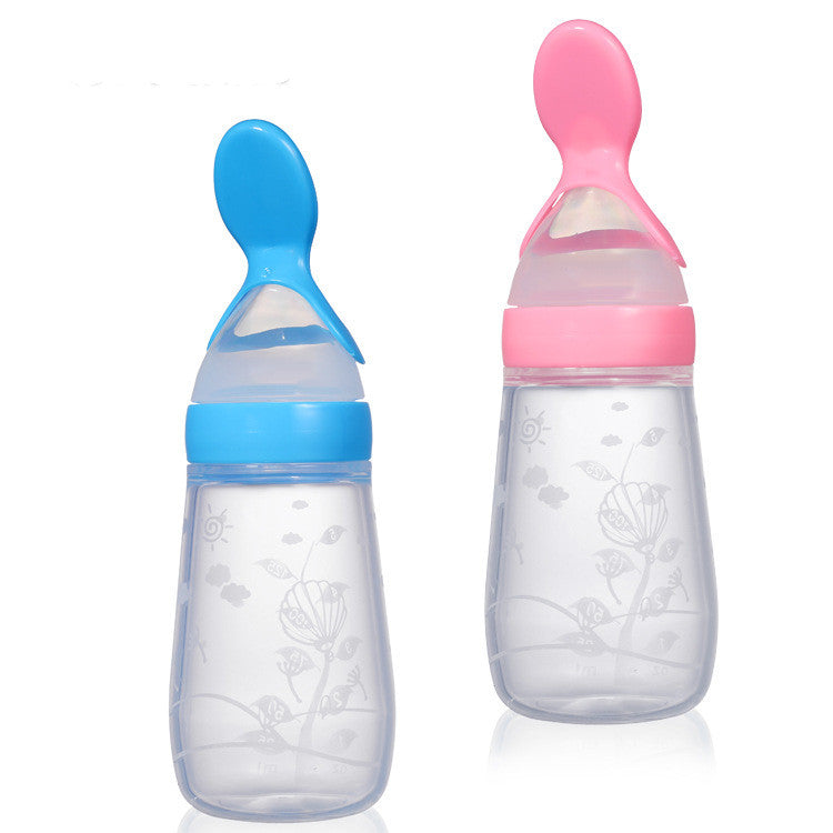 Two transparent baby bottles with floral patterns, one with a blue cap and spoon, the other with a pink cap and spoon, standing on a reflective surface.