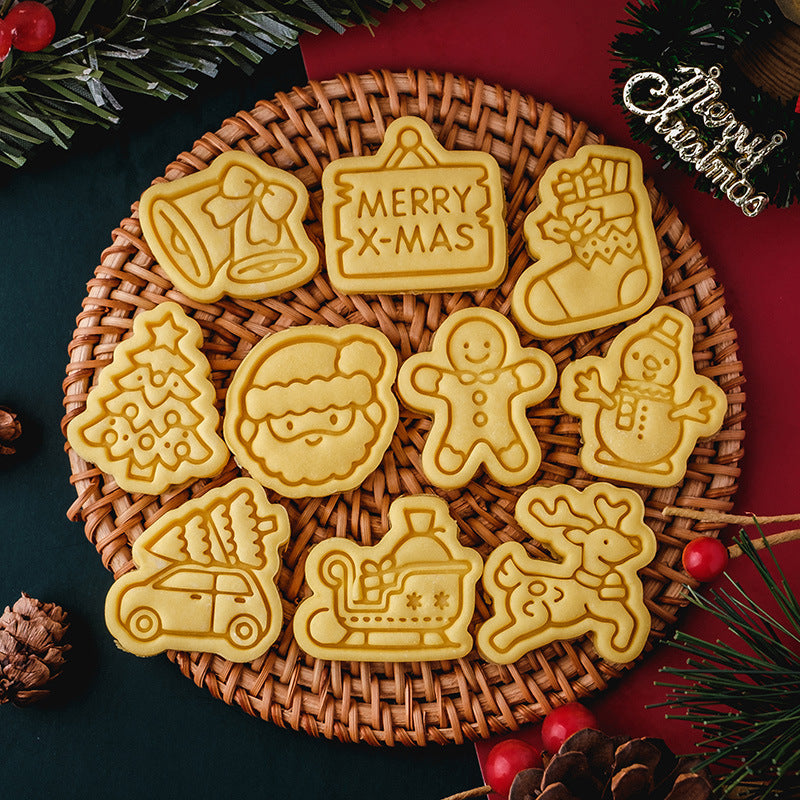 A wicker plate holds Christmas-themed cookies shaped like bells, a tree, Santa, gingerbread man, and more. Pine cones and green branches frame the scene.