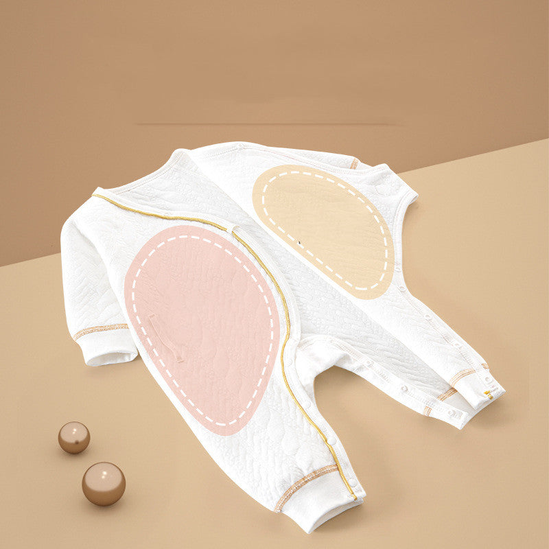 Two white quilted infant onesies with pastel oval patches, one pink and one beige, are arranged on a beige surface. Small beige spheres are nearby.