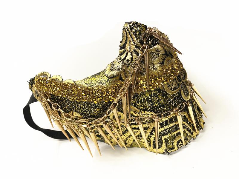 Golden and black ornate mask adorned with sequins, intricate embroidery, and gold chains featuring sharp spikes, creating a dramatic and bold fashion statement.