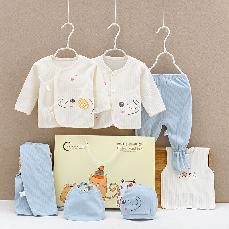 Two baby outfits hang on hangers: cream tops with animal faces and light blue pants. A bib, hat, and extra clothing pieces are below, next to a beige gift box with cat illustrations.