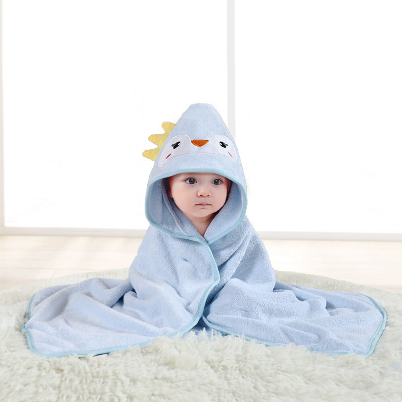 A baby sits on a soft rug wrapped in a light blue hooded towel with a cute animal face design. The background features a bright, soft-lit room.