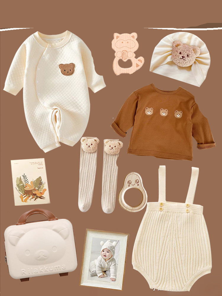 Baby clothing set with teddy bear theme includes a cream onesie, brown top, and cream romper. Accessories: socks, hat, teether, suitcase, book, and framed photo of a baby.