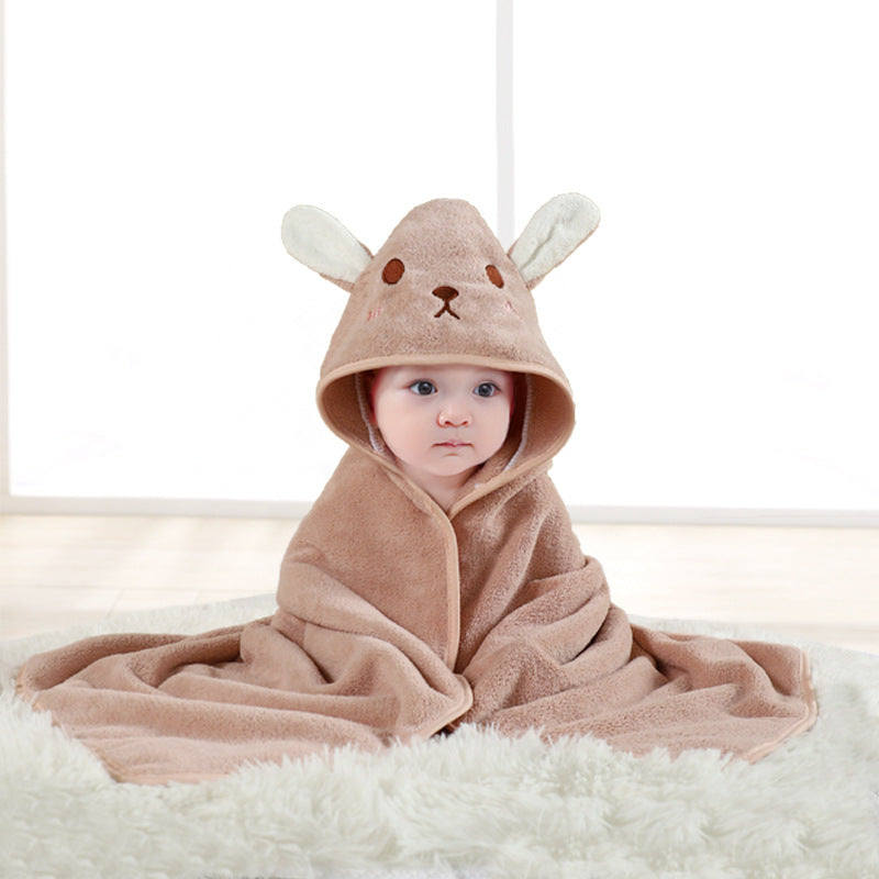Baby wrapped in a soft, brown hooded blanket with bunny ears, sitting on a fluffy white rug in a bright room.