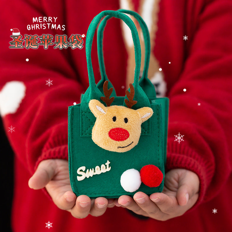 Hands holding a small green felt bag with a reindeer face, labeled "Sweet," featuring red and white pom-poms. Background shows snowflakes and "Merry Christmas" text.