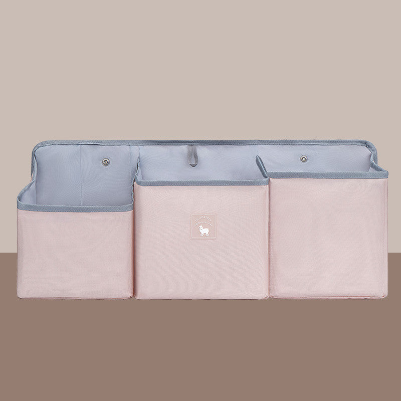 Pink fabric storage organizer with three compartments and gray lining, featuring a small white dog emblem in the center. The background is a soft beige.