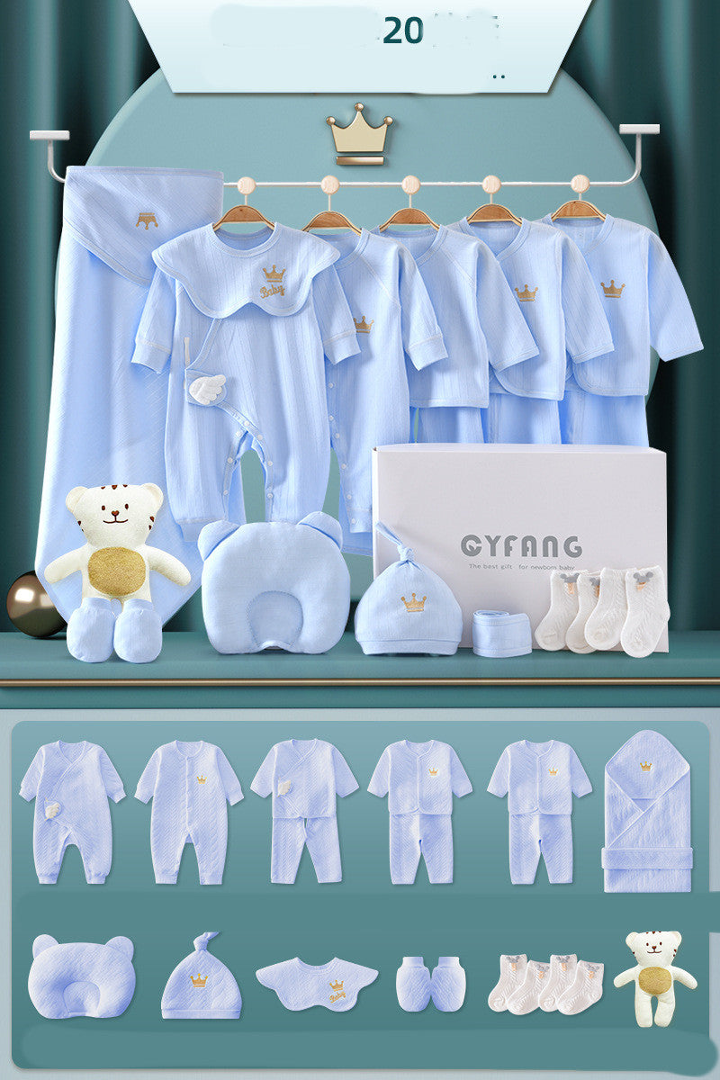 Blue baby gift set with clothing items, soft toy, hat, socks, and blanket, featuring crown and bear designs. Displayed on hangers and a box, arranged neatly on a shelf.