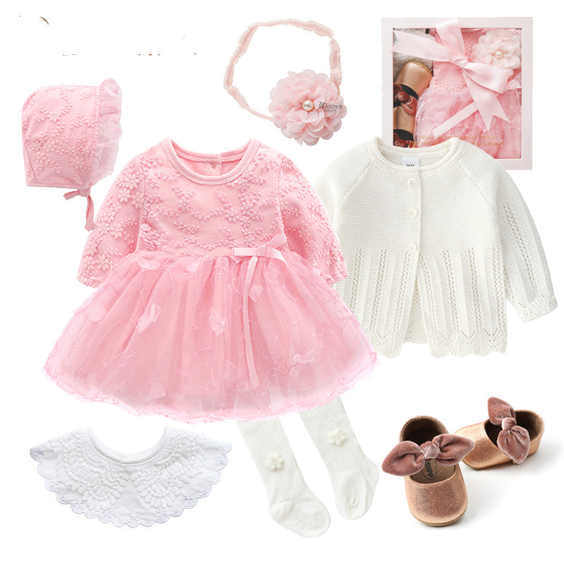 A baby girl outfit set includes a pink lace dress, matching bonnet, floral headband, and white knitted cardigan. Accessories: white tights, lace bib, and brown shoes with bows.