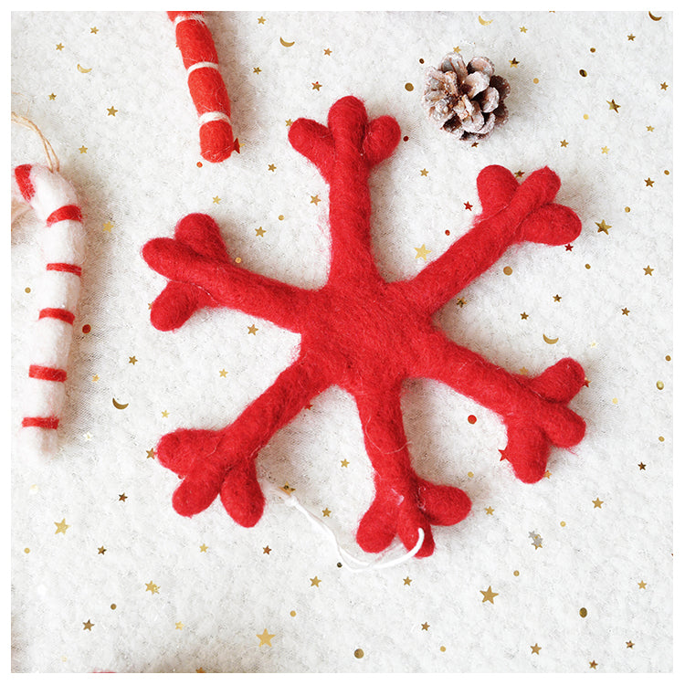 Felt red snowflake ornament on a white fabric background with gold stars, surrounded by candy cane decorations and a pinecone.