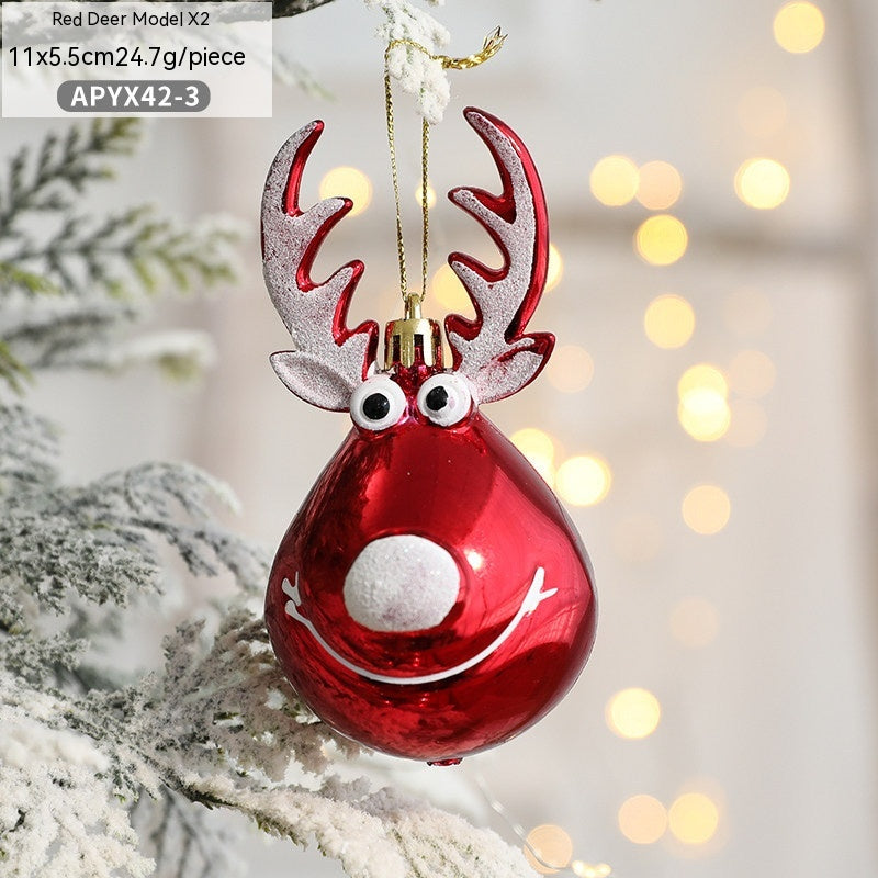 Red deer-shaped Christmas ornament hanging on a tree, featuring googly eyes and a smiling face. The background is softly blurred with warm lights, creating a festive atmosphere.