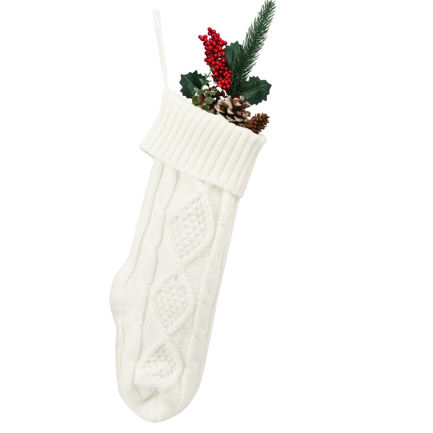 White knitted Christmas stocking with cable pattern, filled with festive decorations including red berries, pinecones, and greenery, hanging against a plain background.