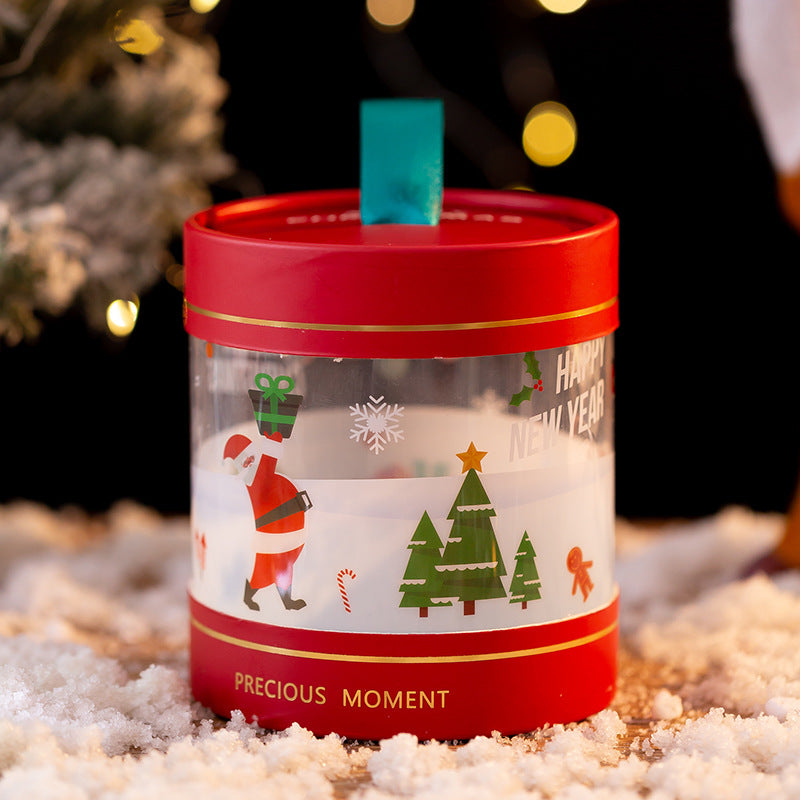 Festive red and clear holiday container with a teal ribbon handle, adorned with Santa, snowflakes, trees, and "Happy New Year" text. Snowy surface and blurry lights in background.