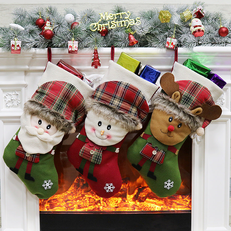 Three festive Christmas stockings shaped like Santa, a snowman, and a reindeer hang over a decorated fireplace with colorful baubles and a "Merry Christmas" sign.