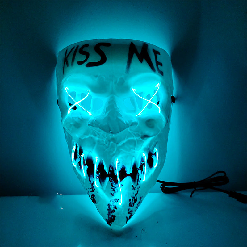 A glowing Halloween mask with neon blue lights outlines a skull face and cross-stitched eyes. "Kiss Me" is written above the brow. A power cord extends from the side.