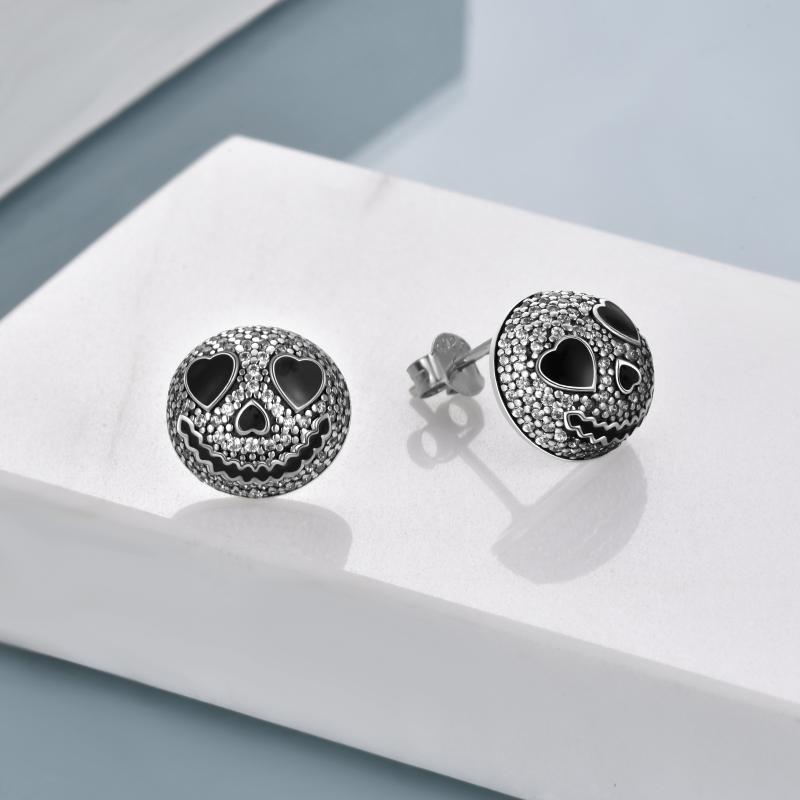 Round stud earrings with black heart-shaped eyes and a smiling face inlaid with small sparkling stones, displayed on a white surface with a light blue background.