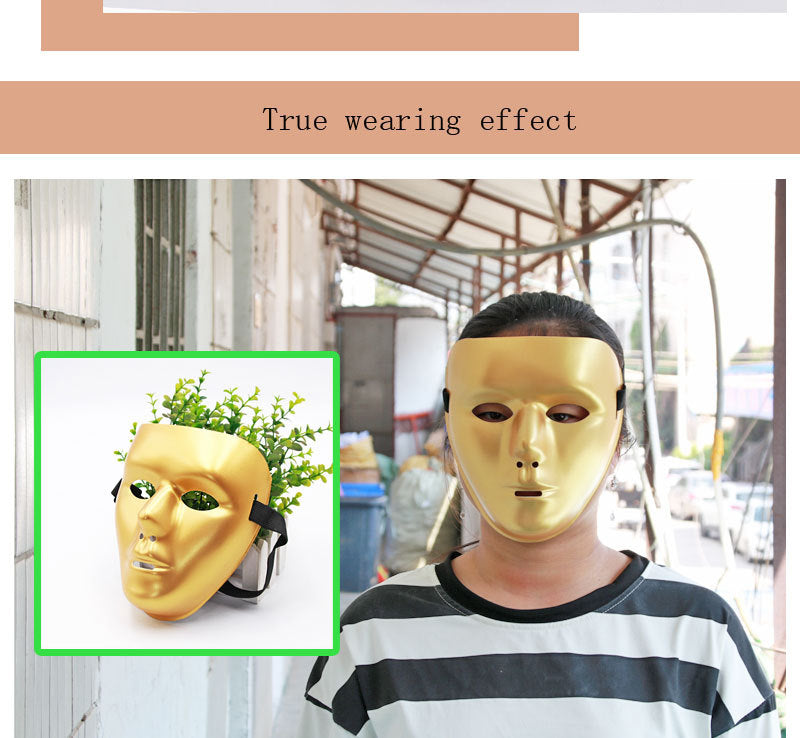 Person wearing a shiny gold mask with a smooth, featureless design. The mask covers the entire face. The background features an industrial setting with scaffolding.