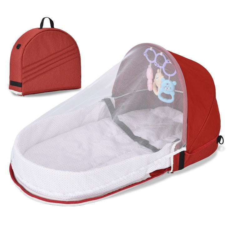 Red portable baby bed with a white mattress and mesh canopy, featuring hanging toys. Includes a matching red carrying case with a handle for easy transport.