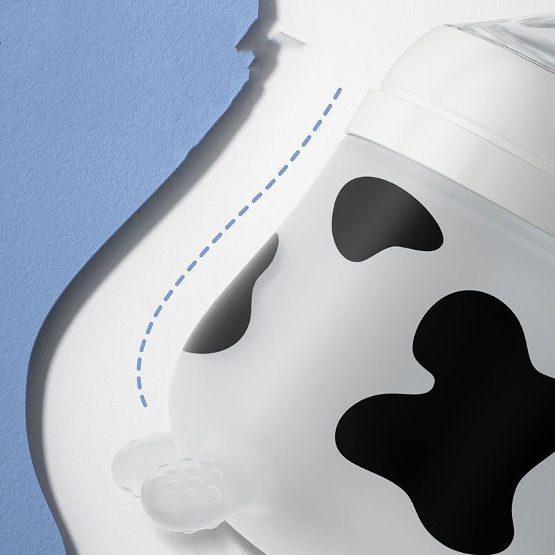 Close-up of a baby bottle with a cow pattern, featuring black spots on a white surface. A textured blue and white background with a dashed blue line adds a playful touch.