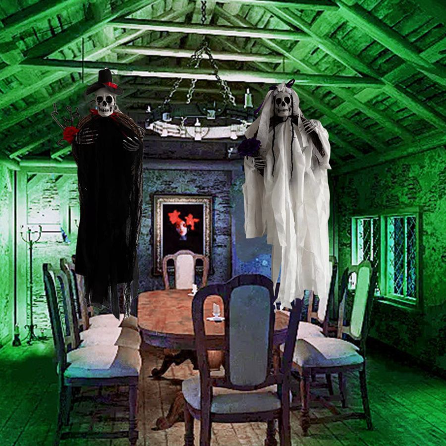 A spooky dining room with a wooden table surrounded by chairs. Two life-sized skeleton figures dressed in wedding attire, a groom in black and a bride in white, are suspended above. The room is illuminated by green lighting and features an eerie portrait on the back wall.