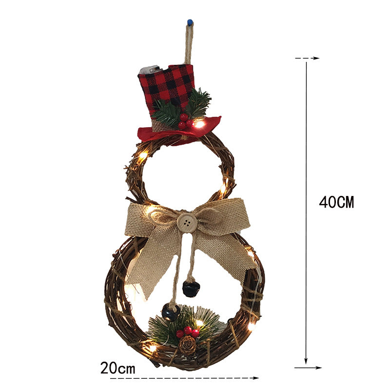 Snowman wall decoration crafted from intertwined twigs with a red plaid top hat, burlap bow, and berry accents. Measures 40cm high and 20cm wide, illuminated with small string lights.