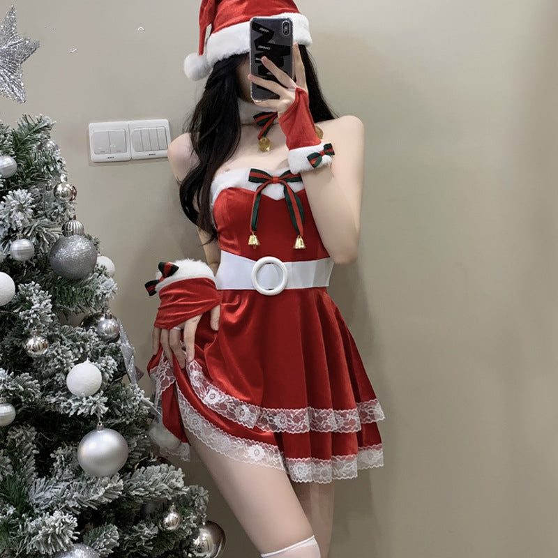A person wearing a red Santa-themed outfit with white fur trim, holding a smartphone in front of a decorated Christmas tree. The outfit features lace and ribbon details.