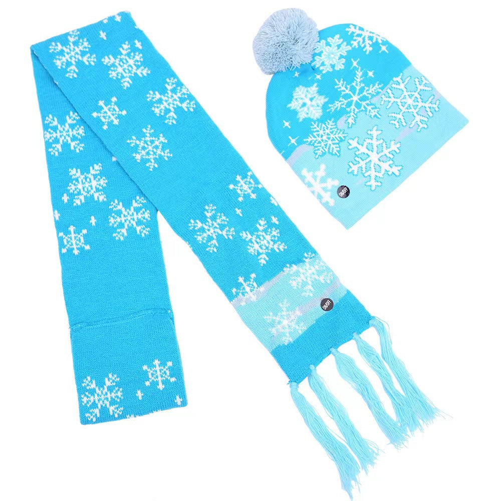 Bright blue knit scarf and beanie set with white snowflake patterns. The scarf has fringed ends, and the beanie features a light blue pom-pom.