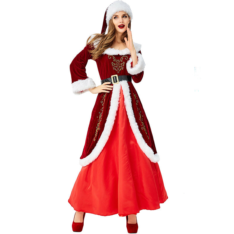 Woman in a Santa-inspired dress with white fur trim, red velvet coat, and belt. She poses with hand on her chin and wears red heels and a matching Santa hat.