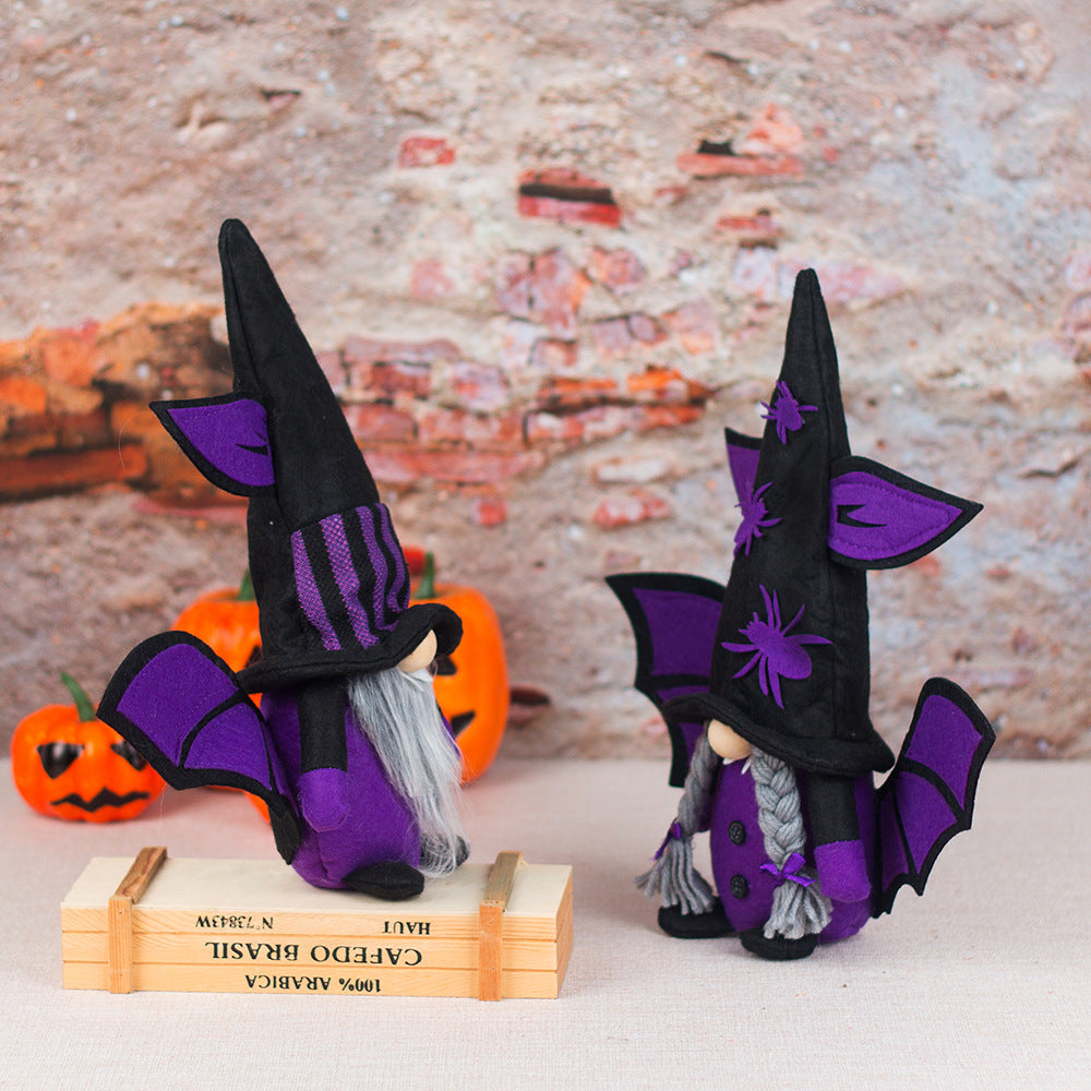 Two whimsical gnome figurines dressed as witches with tall black hats are on display. Each hat features purple bat ears and accents. One gnome stands on a wooden box. Behind them are small carved pumpkins and a rustic brick wall, creating a festive Halloween atmosphere.
