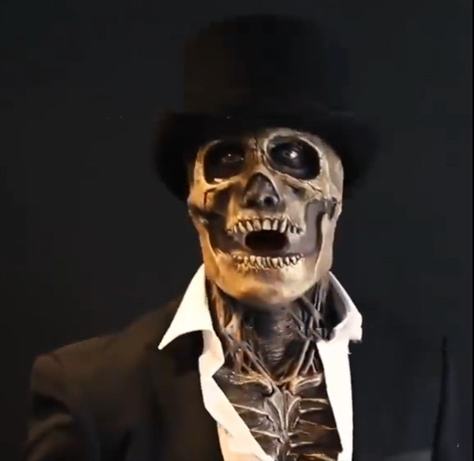 A skull-faced figure in a black suit and top hat with an open collar, against a dark background, giving a mysterious and eerie expression.