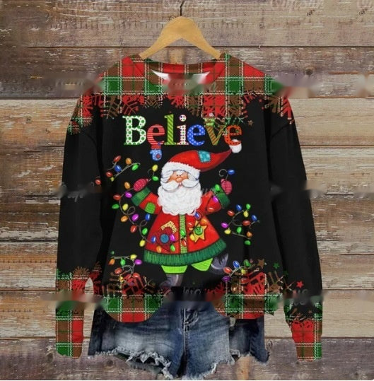 Festive sweater featuring Santa with Christmas lights and the word "Believe," adorned with red and green plaid accents, paired with denim shorts, on a wooden backdrop.