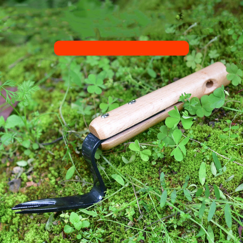 Gardening hand tool with a wooden handle and a metal forked end, resting on lush green moss with small leaves scattered around.