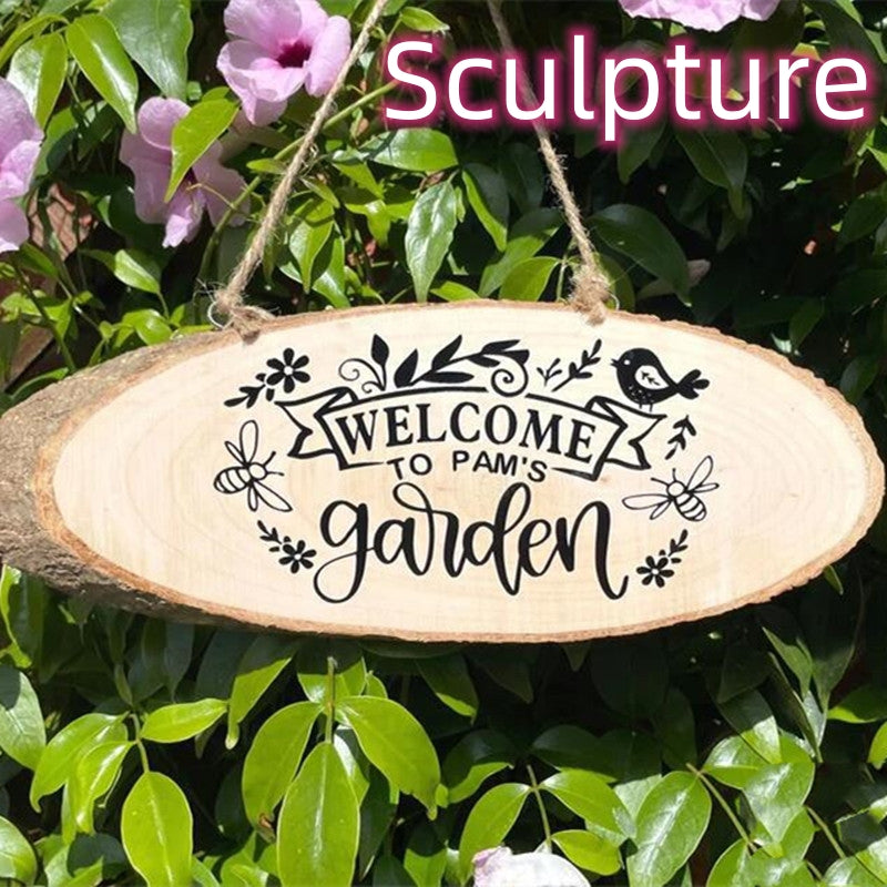 Hanging wooden sign with "Welcome to Pam's Garden" surrounded by floral designs, bees, and a bird. Purple flowers and green leaves in the background.