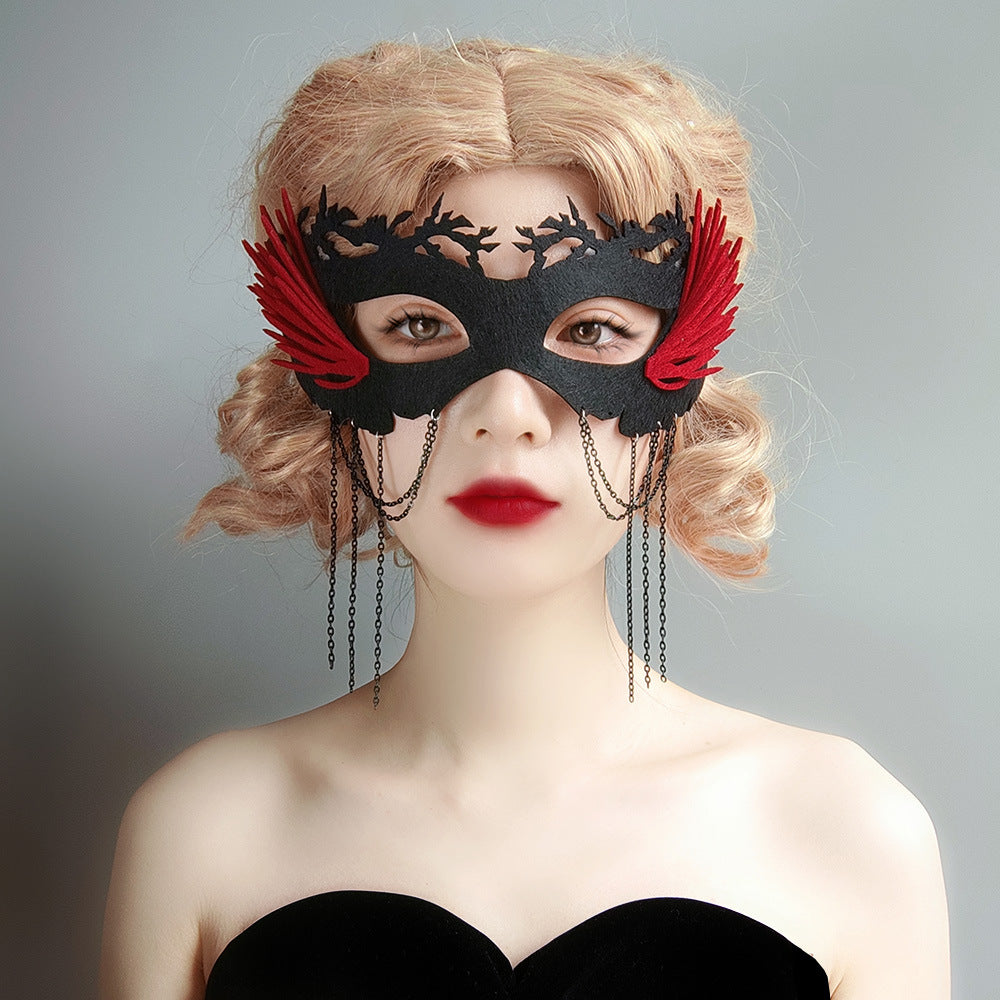 A woman with curly blonde hair wearing an elaborate black and red lace mask with feather accents and hanging chains, styled with a strapless black dress.