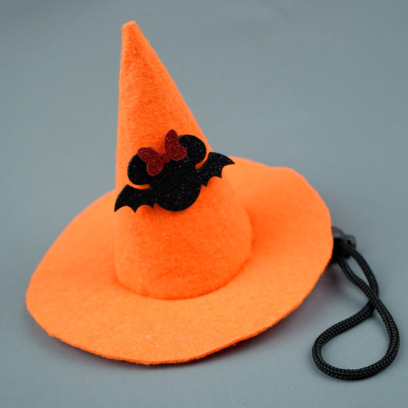 Orange witch hat with a black bat decoration featuring a red bow, on a gray background. The hat includes a black chin strap.
