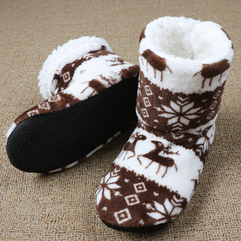Cozy white and brown winter slippers with reindeer and snowflake patterns, featuring plush interiors and black non-slip soles, placed on a textured beige carpet.