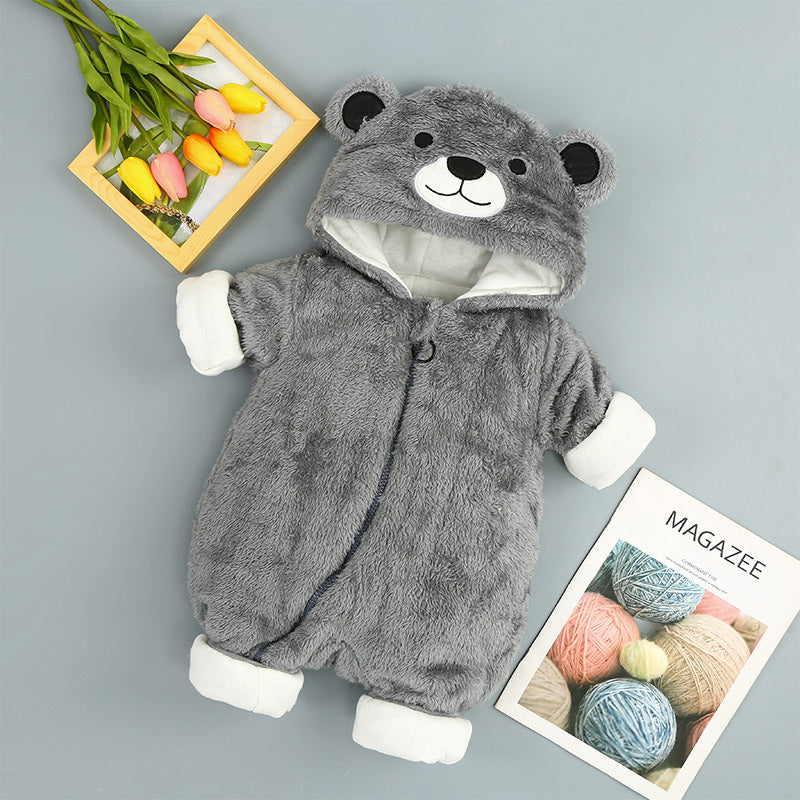 A gray baby onesie with a bear face hood lies on a surface next to a bunch of tulips in a wooden frame and a magazine with colorful yarn balls on the cover.