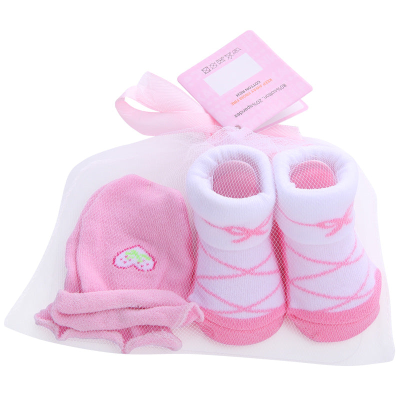 Pink baby gift set with ballet-themed socks, a beanie featuring an embroidered strawberry, and mittens, all wrapped in a delicate white mesh bag with a pink ribbon and tag.