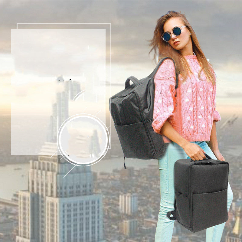 A woman in sunglasses and a pink sweater stands against a cityscape, holding a black backpack and suitcase. The city features tall, blurred skyscrapers in the background.