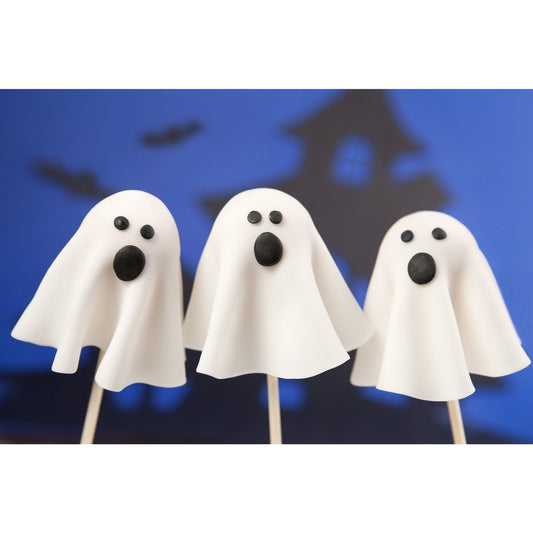 Three ghost-shaped cake pops with white cloth-like coverings and black eyes and mouths against a blue Halloween-themed background with bat and haunted house silhouettes.