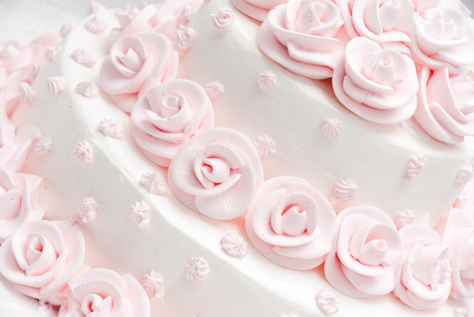 Close-up of a white cake adorned with delicate pink icing roses and small decorative swirls, creating an elegant and intricate design.