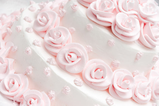 Close-up of a white cake adorned with delicate pink icing roses and small decorative swirls, creating an elegant and intricate design.
