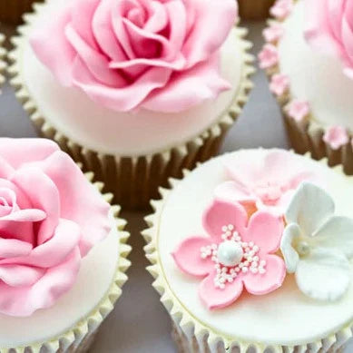 Delicate cupcakes adorned with intricate pink and white icing flowers, including roses and blossoms, arranged in a neat pattern, showcasing elegant craftsmanship and pastel colors.