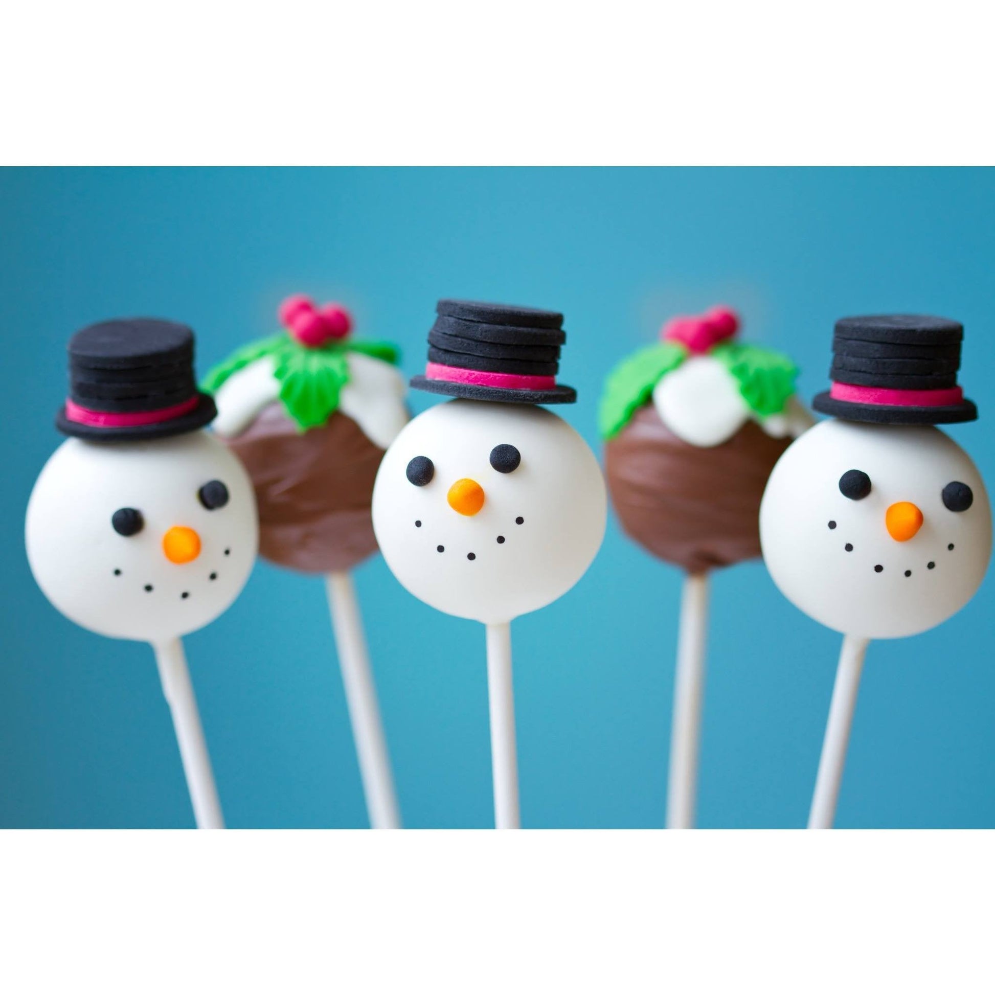 Snowman cake pops with black hats and orange noses on white sticks, alongside chocolate cake pops decorated with white icing, holly leaves, and red berries, set against a blue background.